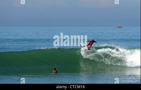 Bärtiger Mann Surfen eine Welle rot Superhelden-Kostüm tragen. Stockfoto