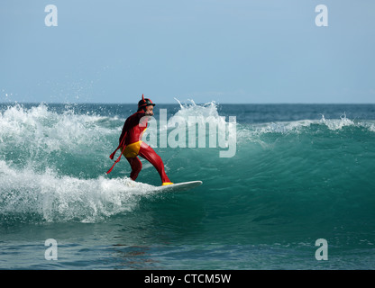 Bärtiger Mann Surfen eine Welle rot Superhelden-Kostüm tragen. Stockfoto