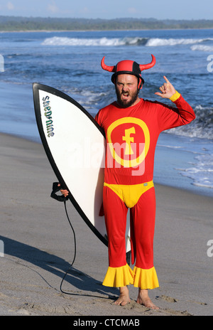 Seltsame Surfen Mann mit Surfbrett in einem roten Superhelden-Anzug an einem tropischen Strand in Sumatra, Indonesien. Stockfoto