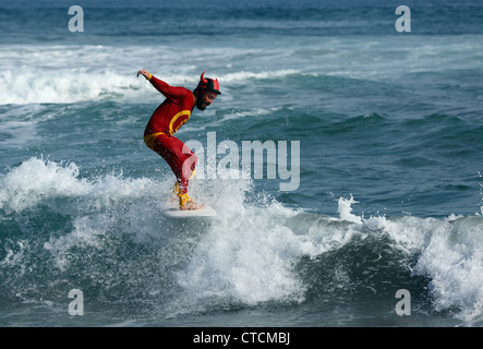 Bärtiger Mann Surfen eine Welle rot Superhelden-Kostüm tragen. Stockfoto