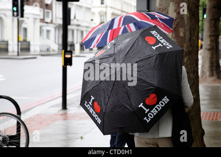 Regen in London, Touristen mit Regenschirmen auf einer Straße im Sommer, England, Großbritannien Stockfoto