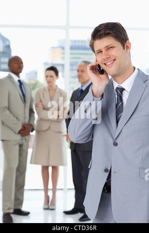 Lächelnd Geschäftsmann mit einem Mobiltelefon vor seinem team Stockfoto