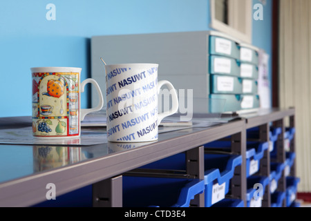 Lehrer Tassen im Lehrerzimmer der Schule, blauer Hintergrund und Rack mit Tabletts / Dateien im Hintergrund unscharf. UK Stockfoto