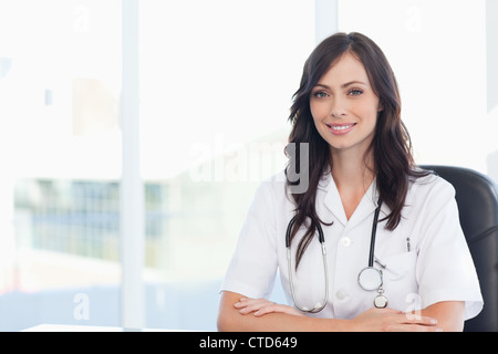 Junger Arzt mit ihren verschränkten Armen auf einem schwarzen Stuhl am Schreibtisch sitzen Stockfoto