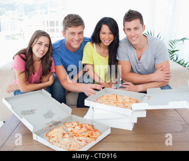 Vier Freunde Lächeln und die Kamera zu stellen, wie sie vor Pizza sitzen Stockfoto
