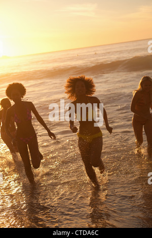 Vier junge Frauen laufen im Wasser bei Sonnenuntergang Stockfoto