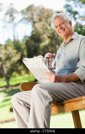 Lächelnde Greis hält eine Zeitung setzt sich Stockfoto
