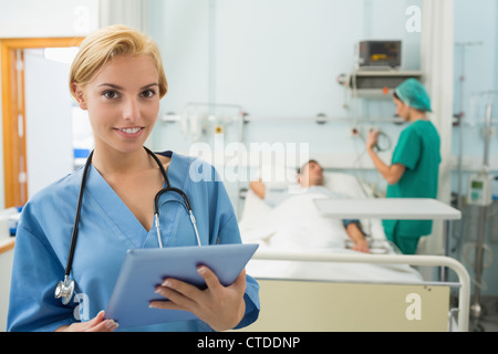 Blonde Krankenschwester hält einen Tabletcomputer während lächelnd Stockfoto