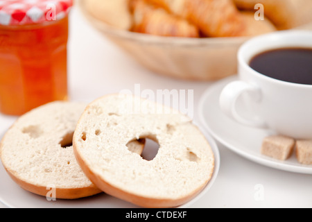 Donut in zwei Hälften geschnitten und eine Tasse Kaffee auf weißen Tellern mit Zucker und Milch und einen Topf mit Marmelade Stockfoto