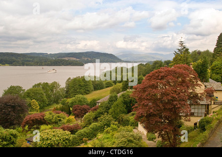 Ein schöner Garten eines Hauses am Rande des Lake Windermere, an dem ein Boot überquert wird. Seenplatte, Cumbria, England, UK. Stockfoto