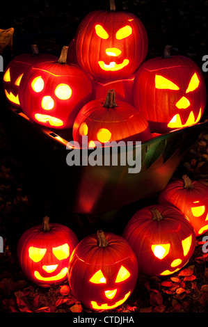 Geschnitzte Kürbisse beleuchtet in einer Schubkarre mit Herbstlaub auf Hinterhof Rasen in der Dämmerung. Stockfoto