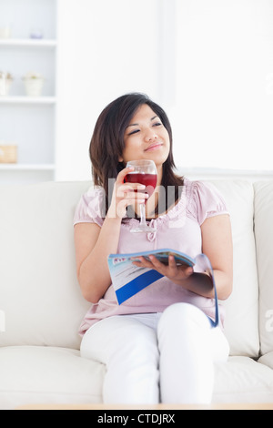 Beim Sitzen auf einem Sofa und hält ein Glas Wein lächelnde Frau Stockfoto