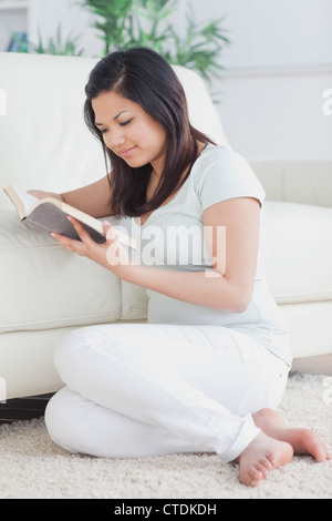 Frau, ein Buch zu lesen, während sie auf dem Boden sitzt Stockfoto