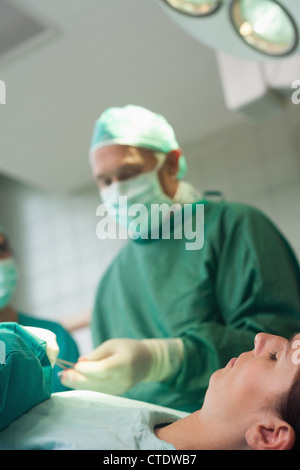 Patienten, die auf eine OP-Tisch zu schlafen, während ein Chirurg Schere stattfindet Stockfoto