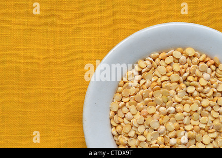 Viele trockene Erbsen Bohnen in weiß Schüssel über gelbe Tischdecke Hintergrund Stockfoto