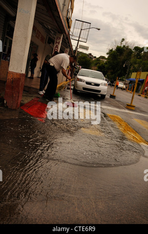 Ein Mann kehrt Wasser aus einer Straße, die einst mit amerikanischen Touristen in Nogales, Sonora, Mexiko beschäftigt war. Stockfoto