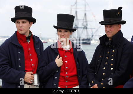 United States Coast Guard, die Seeleute in 1812 Uniformen auf einem Pier, als die USS Constitution, Hintergrund Segel im Hafen von Boston stehen Stockfoto