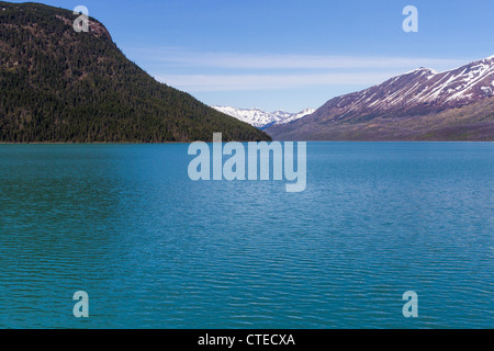 Türkisfarbenes Wasser des Kenai Lake mit schneebedeckten Kenai Mountains in der Ferne, auf der Kenai Peninsula, Alaska, von der Alaska Railroad Zugfahrt aus gesehen. Stockfoto