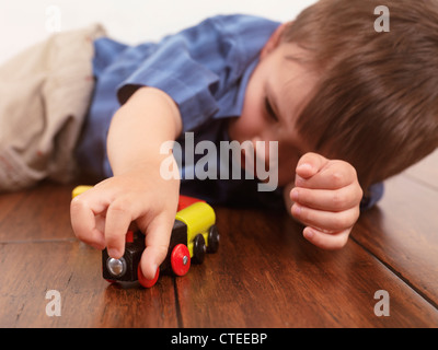 Junge spielt mit einer Spielzeugeisenbahn auf Hartholz-Fußboden liegend Stockfoto