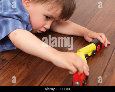 Zwei Jahre alter Junge spielt mit einer Spielzeugeisenbahn auf Hartholz-Fußboden liegend Stockfoto