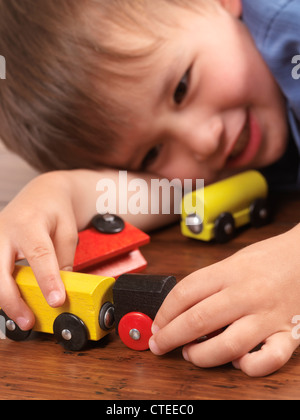 Glücklich zwei Jahre alten Jungen spielen mit einem bunten Spielzeugzug auf Parkett Stockfoto