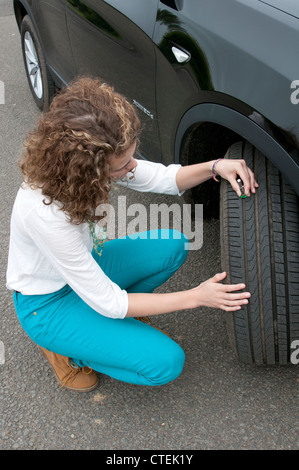 Junge Fahrerin überprüfen Reifen Tiefe auf einem Auto-Rad Stockfoto