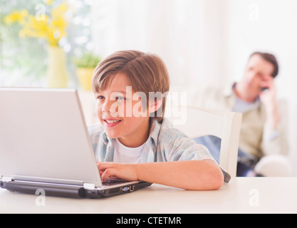 USA, New Jersey, Jersey City Boy (10-11 Jahre) mit Laptop am Tisch mit Vater sitzt im Hintergrund Stockfoto