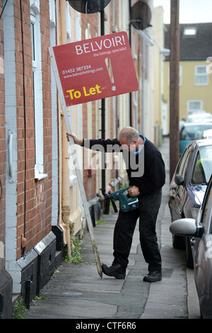 Ein Arbeiter von einer Vermietungsagentur behebt ein Zeichen "Zu lassen", um eine Immobilie in Gloucester UK Stockfoto