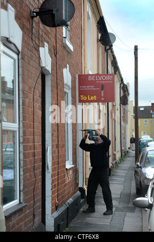 Ein Arbeiter von einer Vermietungsagentur behebt ein Zeichen "Zu lassen", um eine Immobilie in Gloucester UK Stockfoto