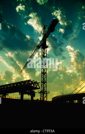 Silhouetten der Baukran und eine Brücke in Dämmerung gegen den bunten Himmel. Stockfoto