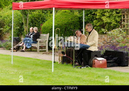 Zwei Männer sitzen unter einem roten Baldachin rund um Musik zu spielen; ein paar saß auf einer öffentlichen Bank in der Ferne Stockfoto