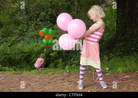 Ein kleines Mädchen im gestreiften Kleid ist rosa Ballons halten. Stockfoto