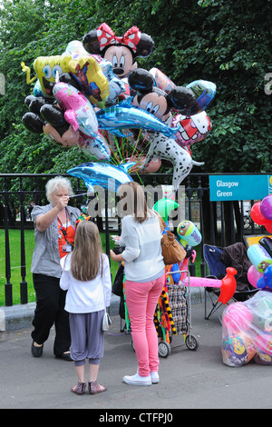 Junges Mädchen mit Mutter Kauf eines Helium Ballon von Anbieter im Glasgow, Glasgow Green Stockfoto