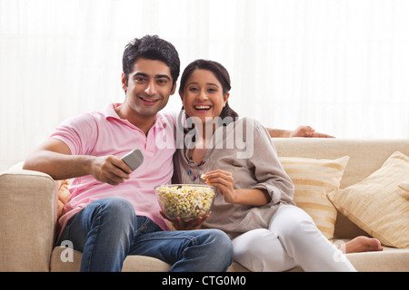 Lächelnd junges Paar vor dem Fernseher während des Essens popcorn Stockfoto
