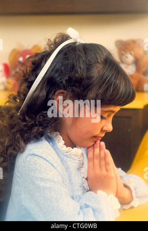 1980ER JAHRE KLEINE MÄDCHEN BETEN AM KRANKENBETT VOR DEM SCHLAFENGEHEN Stockfoto