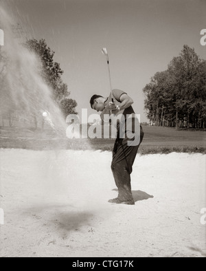 1960ER JAHRE MANN SPIELT GOLF CHIPPING GOLFBALL AUS EINEM SANDFANG IM FREIEN Stockfoto