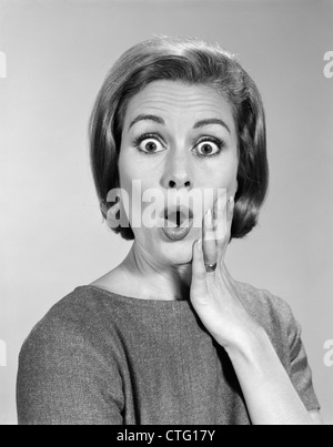 1960ER JAHRE PORTRAIT FRAU MIT HAND AUF WANGE BLICK IN DIE KAMERA MIT SCHOCKIERT AUSDRUCK Stockfoto