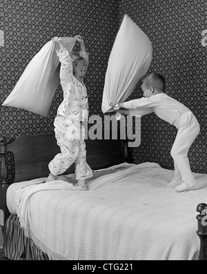 1950ER JAHRE JUNGE & MÄDCHEN BRUDER & SCHWESTER IN PYJAMAS HABEN KISSEN KÄMPFEN AUF BETT Stockfoto