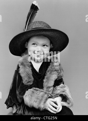 1940ER JAHRE MÄDCHEN IN ÜBERGROßEN SAMT KLEID HUT & PELZE MIT AUGEN BESETZUNG ZUR SEITE & ZUNGE TEILWEISE HERAUS Stockfoto