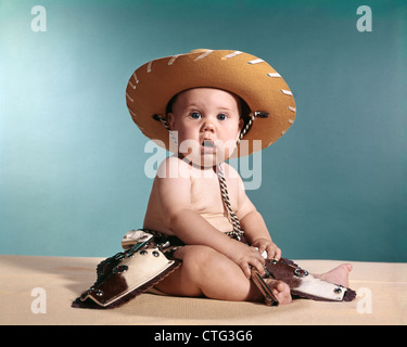 1960ER JAHRE BABY TRAGEN COWBOY KOSTÜM MIT LUSTIGEN GESICHTSAUSDRUCK, BLICK IN DIE KAMERA Stockfoto