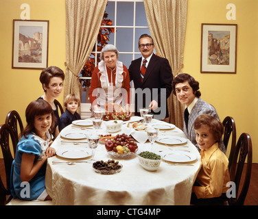 1970ER JAHRE-3 GENERATIONEN-FAMILIE SITZT AM ESSTISCH MIT BLICK IN DIE KAMERA Stockfoto