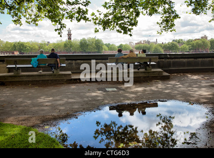 Victoria Gardens Menschen auf Bank und Bäume spiegeln sich in der Pfütze - London UK Stockfoto