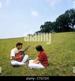1970er Jahren afroamerikanischen paar Mann Frau sitzen auf grasbewachsenen Hügel Mann spielt akustische Gitarre Stockfoto
