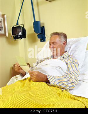 1980ER JAHREN LÄCHELND SENIOR MANN IM KRANKENHAUS BETT ERÖFFNUNG POST BLICK AUF VERSICHERUNG CHECK Stockfoto