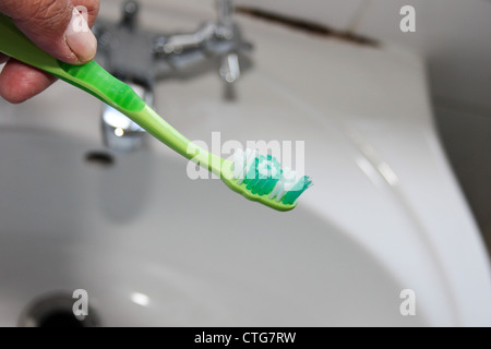 eine Hand hält eine grüne Zahnbürste gegen eine weiße Wanne Nahaufnahme Stockfoto