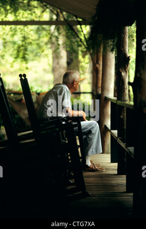 1980ER JAHRE ÄLTERER SENIOR MANN SITZT AUF DER VERANDA IM SCHAUKELSTUHL Stockfoto