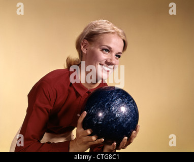 1960ER JAHRE JUNGE LÄCHELND BLONDE FRAU MIT BOWLING-KUGEL TRAGEN ROTE HEMD ÜBER SCHÜSSEL Stockfoto