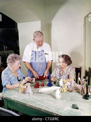 1960ER JAHRE ÄLTEREN MANN UND ZWEI FRAUEN REDEN, GEMEINSAM AUF HANDWERK IM SENIORENHEIM Stockfoto