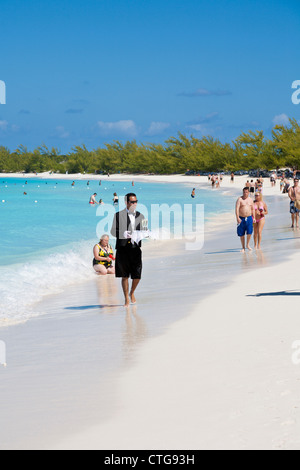 Mann verkleidet als Kellner in Smoking und Shorts mit Champagner am Strand von Half Moon Cay auf den Bahamas Stockfoto