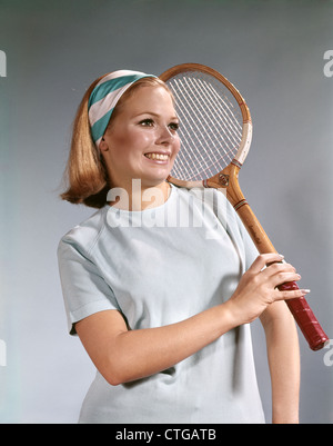 1960ER JAHRE PORTRÄT JUNGEN BLONDEN FRAU HÄLT LÄCHELND TRAGEN BLAU WEIßE STIRNBAND TENNISSCHLÄGER Stockfoto